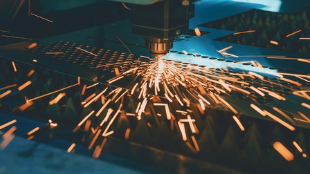 Nahaufnahme eines Lasers, der in eine dünne Metallplatte Löcher lasert