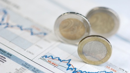 Auf einem Blatt Papier ist eine Tabelle mit Statistikkurven abgedruckt. Auf dem Blatt Papier stehen Euro-Münzen