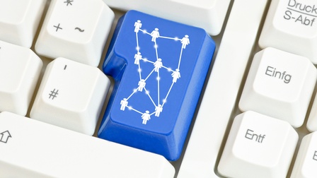 Detailansicht einer Computertastatur, deren Enter-Taste blau und mit Symbolen von Personen versehen ist, die untereinander mit Linien verbunden sind