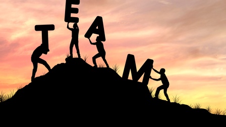 Konzept Team-Work mit Buchstaben, die auf einen Hügel von Personen gemeinsam getragen werden, im Hintergrund zeigt sich eine Abendstimmung