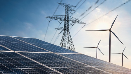Im Vordergrund sind Solaranlagen, daneben stehen ein Strommast und Windräder.
