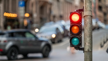 Nahaufnahme einer roten Verkehrsampel auf einer befahreren Straße.
