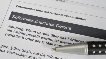 Detailansicht einer Kugelschreiberspitze die auf Dokument mit Schriftzug Soforthilfe-Zuschuss Corona liegt