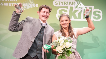 die gewinnerin und der gewinner der styrian skills 2024 halten jeweils einen pokal in die luft und lachen