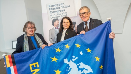 Bundesinnungsmeisterin Christine Schnöll, Landesinnungsmeisterin Anneliese Ringhofer und WKO-Steiermark-Präsident Josef Herk stehen nebeneinander. Gemeinsam halten sie eine Flagge.
