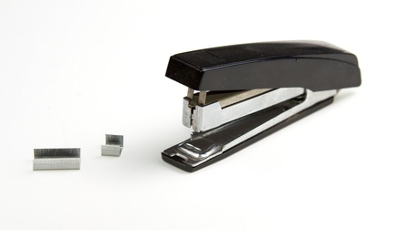 Ein Heftklammern-Tacker vor einem weißen Hintergrund. Neben dem Tacker liegen Heftklammern