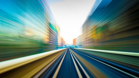 Foto einer Straße in Bewegungsunschärfe. Links und rechts von der Straße sind hohe Gebäude
