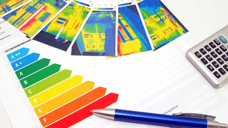 Eine Energieeffizienzskala, Infrarot Wärmebilder von Häusern sowie ein Taschenrechner und ein Kugelschreiber auf einem Tisch