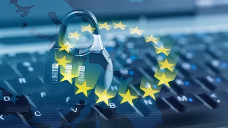 Nahaufnahme eines Ausschnitts einer Computertastatur. Darüber ist eine Karte von Europa gelegt, sowie goldene Sterne in einem Kreis und ein Sicherheitsschloss