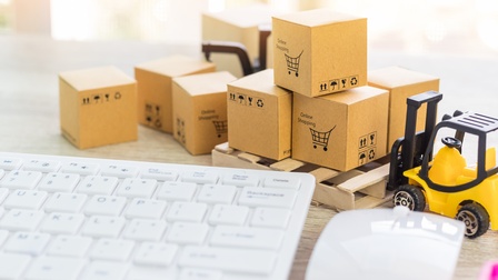 Nahaufnahme des rechten oberen Bereichs einer Tastatur, einer Computermaus, Miniaturkartons, auf denen online shopping steht und eines Miniaturgabelstaplers 