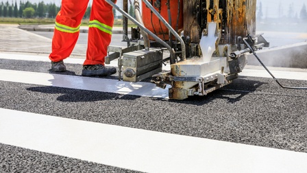 Detailansicht einer Maschine, die von Person geschoben wird, die Farbe auf Straße für Markierungen appliziert