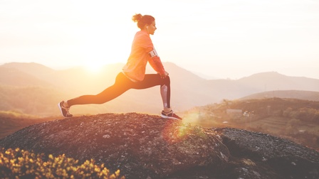 Person dehnt sich im Sonnenuntergang auf Fels stehend