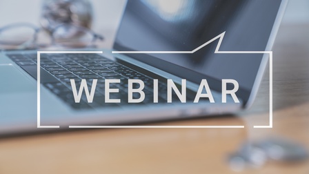 Seitliche Aufnahme eines auf einem Tisch stehenden, aufgeklappten Laptops. Über dem Foto steht in weißer Schrift Webinar in einer Sprechblase