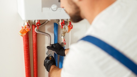 Nahaufnahme von einer Person, die eine Therme wartet und dabei Schutzkleidung trägt