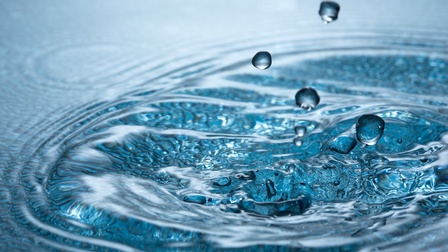 Nahaufnahme eines Wassers, in das ein paar Wassertropfen fallen und Wellen schlägt.