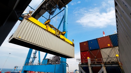 Ein Container wird von einem Kran angehoben, ringsum stehen viele weitere Container