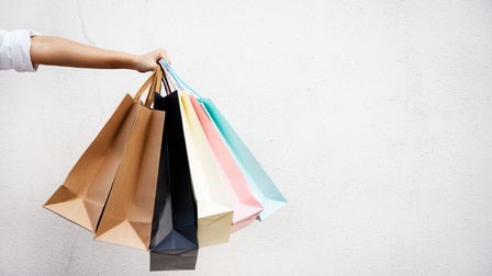 Detailansicht einer Hand, die mehrere Papiertaschen unterschiedlicher Farben hält vor weißem Hintergrund