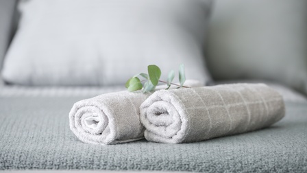 Zwei eingerollte, hellgraue Handtücher auf einem Bett