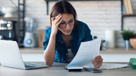 Eine Person sitzt an einem Küchentisch und blickt nachdenklich auf ein Dokument.