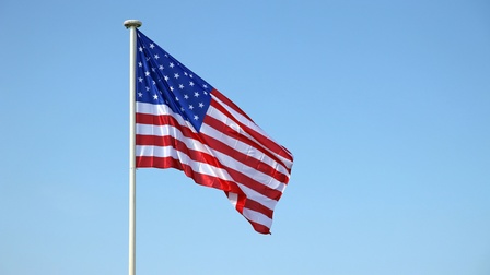An einer Metallstange hängt die Flagge der USA vor einem blauen Himmel