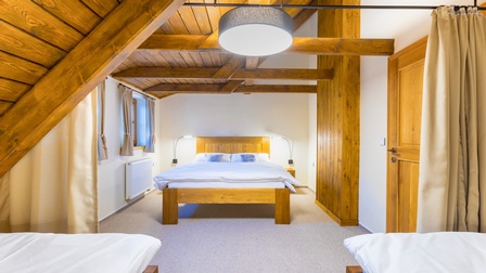 Blick auf ein Schlafzimmer mit Betten aus Holz und Holzverkleidung der Dachschrägen