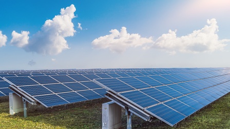 Schräg geneigte Solarpanele auf Wiese stehend unter blauem Himmel mit Wolken