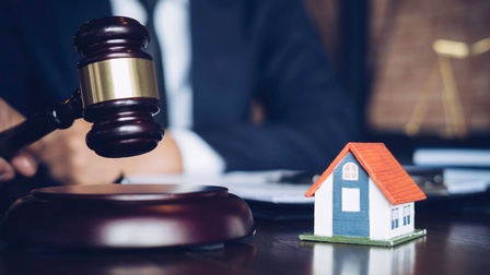 Auf einem Tisch steht ein Modell eines kleinen Hauses. Daneben ist ein Richterhammer