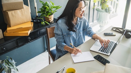 Person mit Brille sitzt an einem Schreibtisch und arbeitet mit einem Laptop