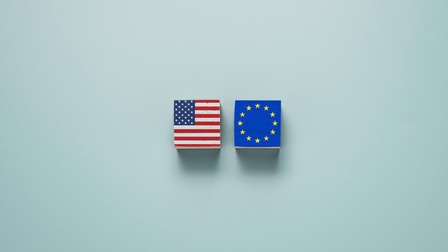 Auf hellblauem Hintergrund liegen zwei Würfel nebeneinander. Auf dem linken Würfel ist die Flagge der Vereinigten Staaten von Amerika. Auf dem rechten Würfel ist die Flagge der Europäischen Union