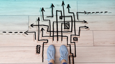 Top-Shot bläulicher Turnschuhe, die auf einem hölzernen Boden stehen. Vor den Schuhen sind grafische, schwarze Pfeile auf dem Boden. Die Pfeile verlaufen kreuz und quer und zeigen in unterschiedliche Richtungen