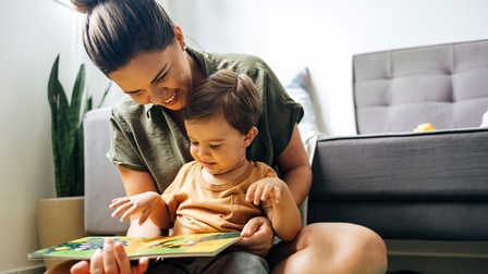 Person sitzt am Boden mit Baby und Bilderbuch