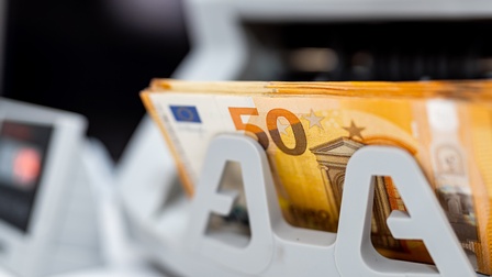 Mehrere 50 Euro Geldscheine liegen in einer Geldzählmaschine