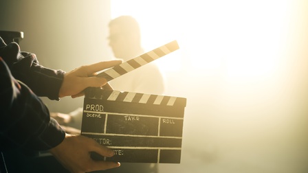 Set mit Fokus auf eine Filmklappe, die von zwei Händen gehalten wird