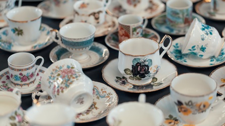 Nahaufnahme verschiedener weißer Tassen mit Blumenmustern und Untertassen mit Blumenmustern auf einem Tisch mit dunklem Tischtuch.