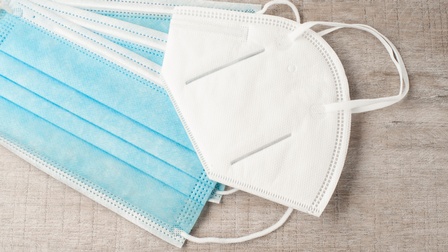 Blaue Mund-Nasen-Schutzmasken sowie eine FFP2-Maske vor einem Holzuntergrund