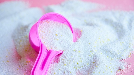 Nahaufnahme von Waschmittel in Pulverform mit einem rosa Messbecher auf einem rosafarbenen Untergrund