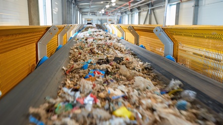 Fließband eingefasst von gelbem Gitter voller Müll in Bewegungsunschärfe