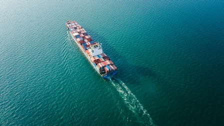 Top-Shot eines großen Schiffes in einem Gewässer, auf dem viele, bunte Container über- und nebeneinander gestapelt sind.