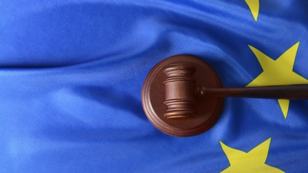 Blauer Stoff mit Falten und gelben Sternen, darauf liegend Richterhammer aus Holz mit kreisrunder Holzfläche