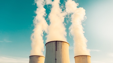 Drei Kraftwerkreaktoren vor blauem Himmel, aus denen Rauch aufsteigt