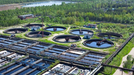 Vogelperspektive einer Wasseraufbereitungsanlage: Runde und viereckige Wasserbecken nebeneinander in grüner Landschaft mit Bäumen