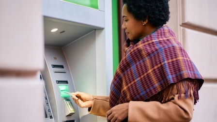 Person mit Winterkleidung steht bei einem Geldautomaten und führt eine Bankomatkarte ein