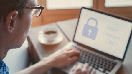 Person mit Brille im Fokus arbeitet an einem Laptop und versucht sich mit einem Passwort einzuloggen