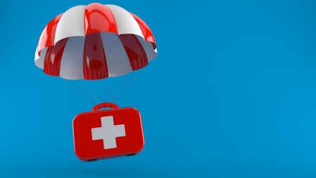 Ein roter Erste Hilfe Koffer mit weißem Logo fliegt mit einem rot-weißen Fallschirm vor einem blauen Hintergrund