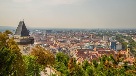 Aufnahme des Grazer Uhrturms aus der Vogelperspektive. Zu Füßen des Uhrturms ist die Stadt Graz sowie der Fluss Mur