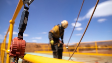 Eine Person in Schutzkleidung steht auf einer Baustelle. Man sieht Kabel und ein Metallgitter. Es herrscht Sonnenschein.