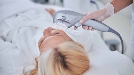 Frau wird kosmetisch mit einem Cavitationsgerät im Gesicht behandelt