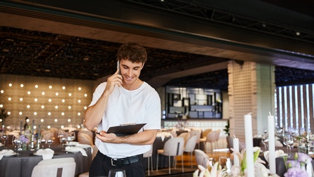 Eine Person telefoniert gerade und hat ein Clipboard in der Hand. Sie befindet sich in einem Raum, der für ein Event vorbereitet wird. 