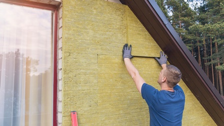 Person in Rückenansicht mit Handschuhen drückt gelbe Dämmplatten an Hausfassade