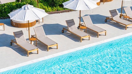 Liegen sowie Sonnenschirme stehen neben einem Pool mit seitlicher Sicht darauf